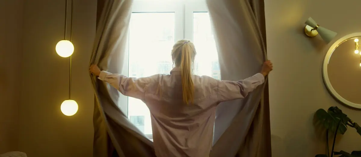 Persona abriendo las cortinas de una ventana