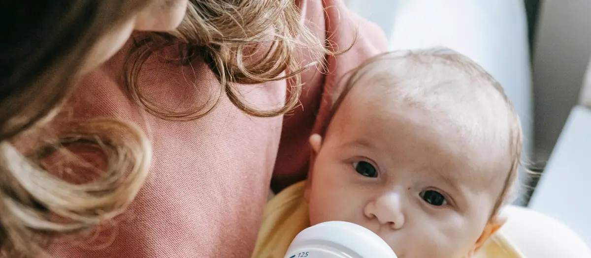 Bebé tomando el biberón en brazos de su madre