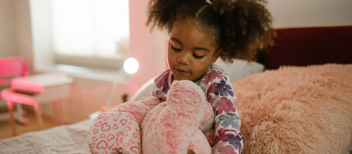 Niña en pijama sentada en la cama con un peluche