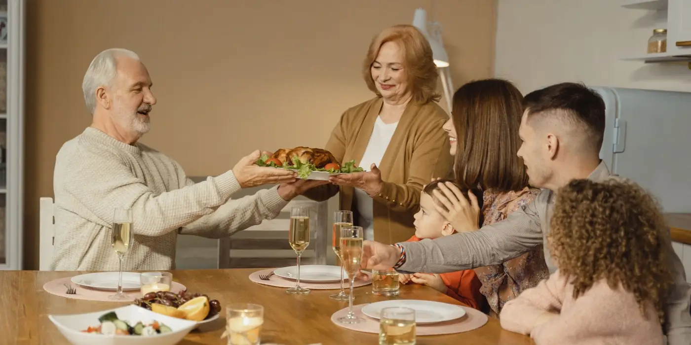 Una familia de varias generaciones come junta en casa, en una mesa de madera con platos de cerámica y vasos de cristal
